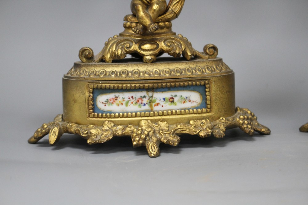 A pair of French gilt metal two light candelabra, modelled with putti seated beneath vine branches and inset with Sevres style